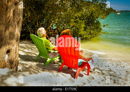 Anonimo coppia Senior godendo la vista dal loro colorate sedie da spiaggia vicino al bordo dell'acqua su una spiaggia di sabbia bianca Foto Stock