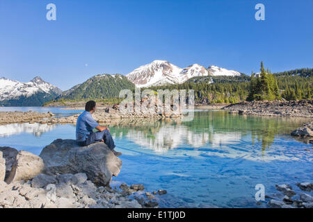 Escursionista guardando una montagna riflessione sul lago Garibaldi, Garibaldi Parco Provinciale nei pressi di Whistler in British Columbia, Canada. Foto Stock