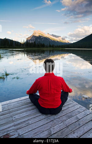 La mezza età uomo meditando sul dock a Vermillion Lake, il Parco Nazionale di Banff, Alberta, Canada. Foto Stock