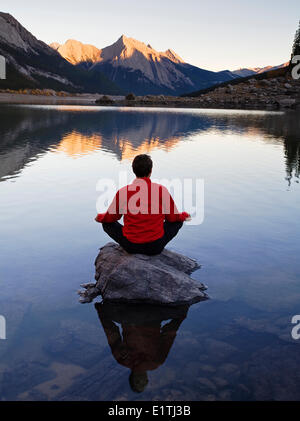La mezza età uomo meditando su roccia sulla medicina Lake, il Parco Nazionale di Jasper, Alberta, Canada. Foto Stock