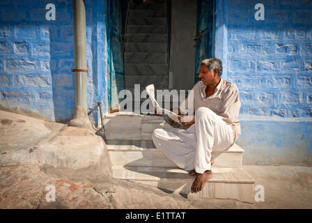 Un uomo legge un giornale sulla sua porta nelle strade di Jodhpur, stato del Rajasthan, India Foto Stock