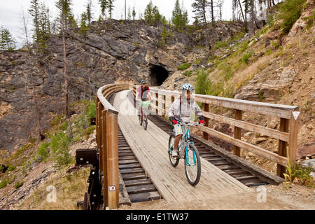 Famiglia giovane in bicicletta il Kettle Valley Railway Trail attraverso Myra canyon, Okanagan Valley, BC, Canada. Foto Stock