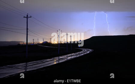 Strada bagnata e poli di utilità illuminata da fulmini in passaggio orientale, Nova Scotia, durante una tempesta di sera. Foto Stock