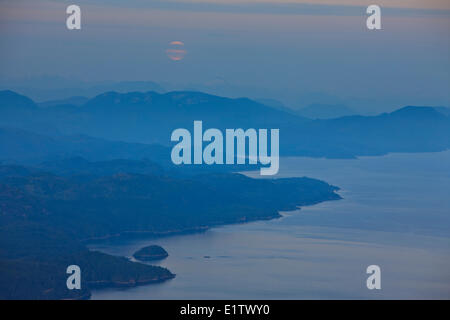 Guardando oltre Johnstone stretto verso la British Columbia montagne costiere con una luna piena sorgere al crepuscolo crepuscolo British Foto Stock