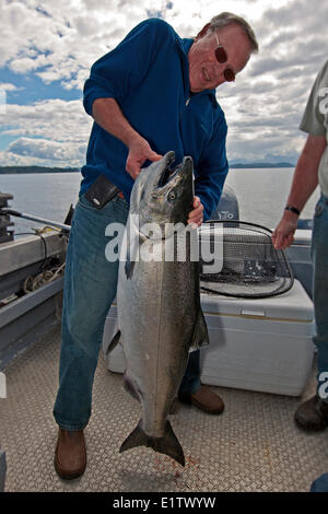Senior pensionati uomo orgoglioso di contenimento di una molla enorme di salmone che ha appena catturati su una piccola barca da pesca fuori del nord Isola di Vancouver Foto Stock