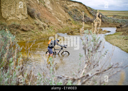 Un uomo spinge la sua mountain bike attraverso la molla run off condizioni sul Maah Daah Hey Trail, North Dakota Foto Stock