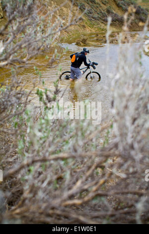 Un uomo spinge la sua mountain bike attraverso la molla run off condizioni sul Maah Daah Hey Trail, North Dakota Foto Stock