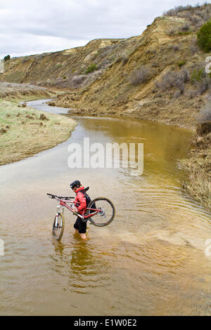Una donna cammina la sua mountain bike attraverso la molla run off condizioni sul Maah Daah Hey Trail, North Dakota Foto Stock