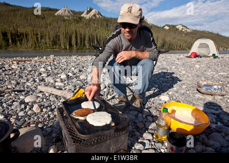 Uomo di mezza età cucinare frittelle su firebox mentre si accampò sul fiume Nahanni, Parco Nazionale Nahanni preservare, NWT, Canada. Foto Stock