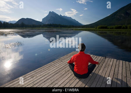 54 enne maschio meditando sul dock presso il lago di Vermillion, Banff, Alberta, Canada Foto Stock