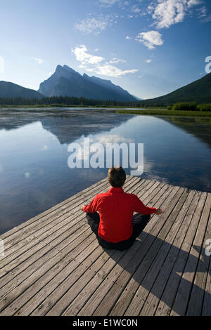 54 enne maschio meditando sul dock presso il lago di Vermillion, Banff, Alberta, Canada. Foto Stock