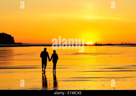 Coppia giovane al tramonto camminando lungo la spiaggia di Chesterman vicino a Tofino, BC. Foto Stock
