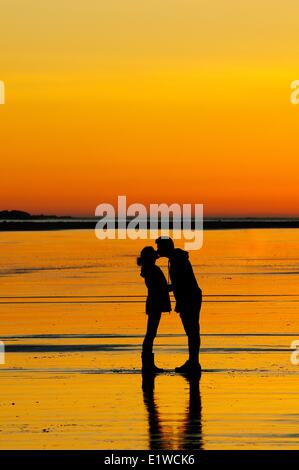 Una giovane coppia al tramonto attorno a baciare mentre sulla spiaggia di Chesterman vicino a Tofino, BC. Foto Stock