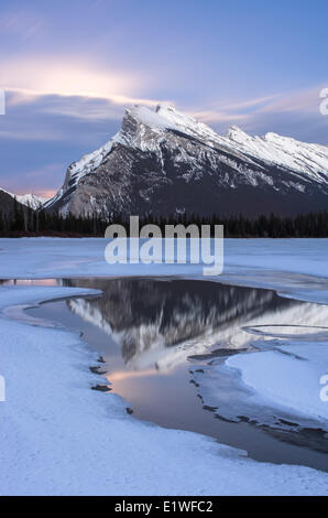 Luna crescente dietro le nuvole dietro Mount Rundle riflettendo in Vermiglio laghi in inverno nel Parco Nazionale di Banff, Alberta, Canada. Foto Stock