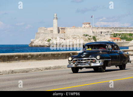 Vintage american cars alomg il Malecon, dietro è Morro Castello, una pittoresca rocca custodisce l'ingresso alla Baia dell Avana, HAV Foto Stock