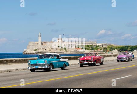 Vintage american cars alomg il Malecon, dietro è Morro Castello, una pittoresca rocca custodisce l'ingresso alla Baia dell Avana, HAV Foto Stock