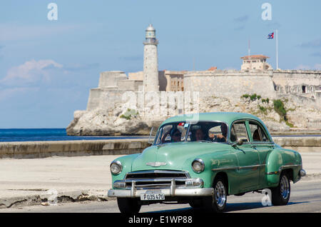 Vintage american cars alomg il Malecon, dietro è Morro Castello, una pittoresca rocca custodisce l'ingresso alla Baia dell Avana, HAV Foto Stock