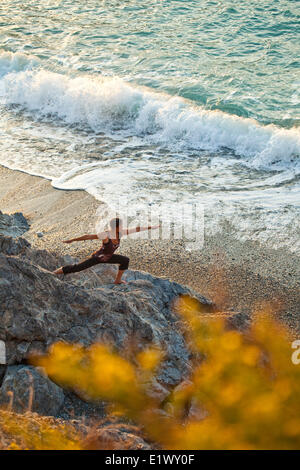 Una giovane donna a praticare lo Yoga al tramonto vicino alla spiaggia a Kalymnos, Grecia Foto Stock