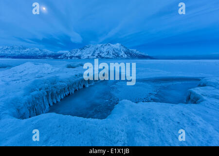 Lago Kluane dopo il ghiaccio ha parzialmente coperto il lago. La luna è visibile sulla montagna di ovini nelle prime ore del mattino. Foto Stock