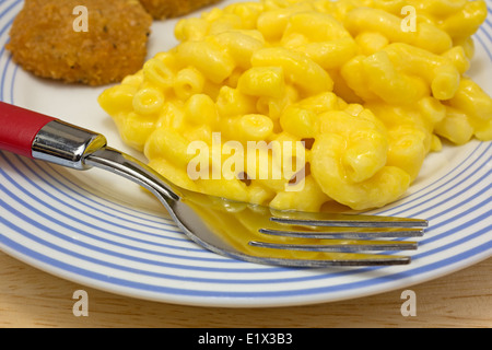 Chiudere la vista di un pasto di pepite di pollo con maccheroni e formaggio su una piastra con la forcella. Foto Stock