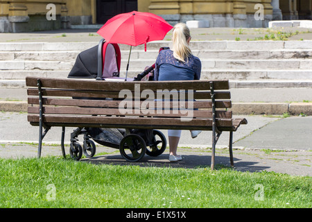 Madri e bambino nel passeggino, seduto su un banco di lavoro Foto Stock