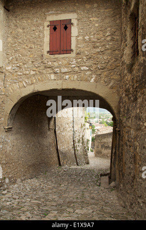 Un acciottolato stretto vicoletto, Rue St François, conduce giù dal Tour de Crest per la città vecchia, passando sotto un arco medievale. La Drôme, Francia. Foto Stock