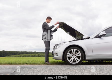Lunghezza piena vista laterale del giovane imprenditore apertura ripartiti auto cofano in campagna Foto Stock