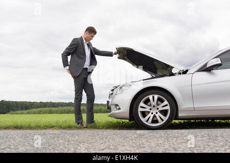 Lunghezza piena vista laterale del giovane imprenditore esaminando ripartiti in auto a motore a campagna Foto Stock