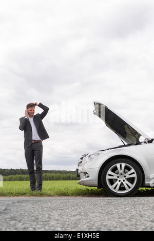 Frustrati giovane imprenditore tramite telefono cellulare vicino ripartiti in auto in campagna Foto Stock