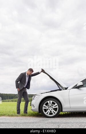 Vista laterale del giovane imprenditore esaminando ripartiti in auto a motore a campagna Foto Stock