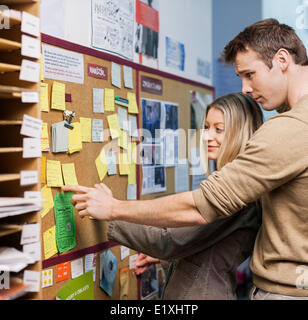 La gente di affari la lettura di promemoria sul bulletin board in office Foto Stock