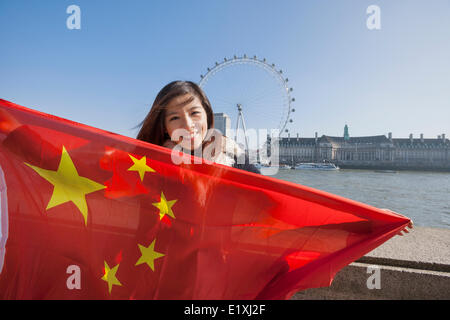 Ritratto di felice giovane donna holding bandiera cinese contro il London Eye a Londra, Inghilterra, Regno Unito Foto Stock