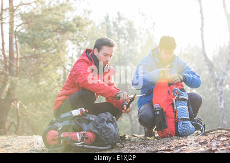 Backpacker maschio con amico whittling legno in foresta Foto Stock