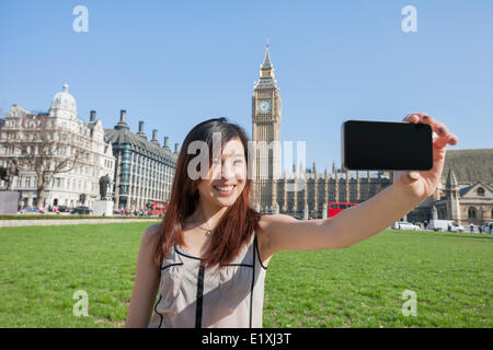 Giovane donna prendendo ritratto di auto attraverso smart phone contro il Big Ben a Londra, Inghilterra, Regno Unito Foto Stock