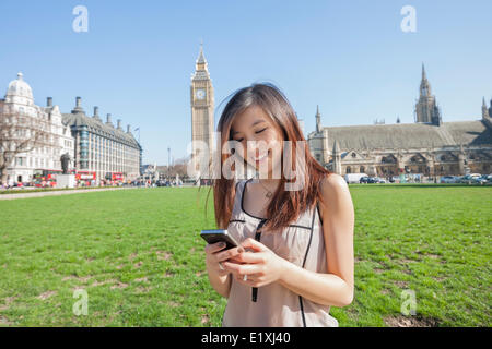 Giovane donna alla messaggistica di testo tramite telefono intelligente contro il Big Ben a Londra, Inghilterra, Regno Unito Foto Stock