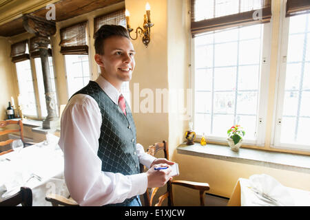 Vista laterale del cameriere con notepad sorridente in ristorante Foto Stock