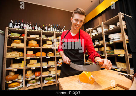 Ritratto di fiducioso venditore maschio formaggio da taglio in negozio Foto Stock