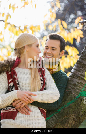 Felice giovane donna abbraccia mentre appoggiata sul tronco di albero in autunno nel parco Foto Stock