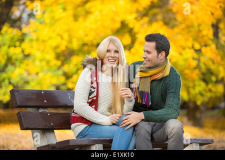 Felice coppia giovane seduto su una panchina nel parco durante l'autunno Foto Stock