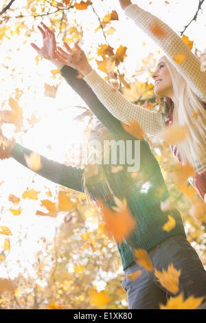 Giovane con le braccia sollevate godendo la caduta di foglie di autunno nel parco Foto Stock