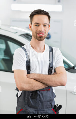 Ritratto di fiducioso tecnico di manutenzione in piedi con le braccia incrociate in officina di riparazione Foto Stock