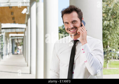 Ritratto di felice giovane imprenditore utilizzando il telefono cellulare al di fuori ufficio Foto Stock