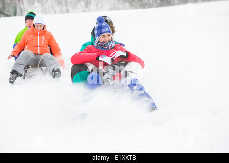 Coppie giovani godendo di sled guidare su strade coperte di neve pendenza Foto Stock