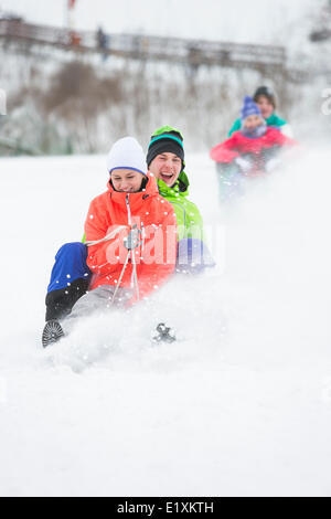 Coppia giovane godendo di sled guidare su strade coperte di neve pendenza Foto Stock