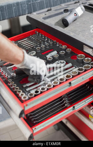 Immagine ritagliata di meccanico maschio tenendo utensile dal cassetto in officina per auto Foto Stock