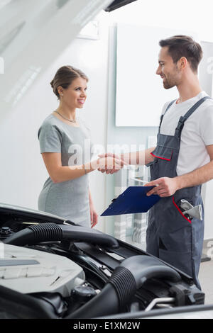 Riparazione giovane lavoratore stringono le mani con il cliente in officina per auto Foto Stock