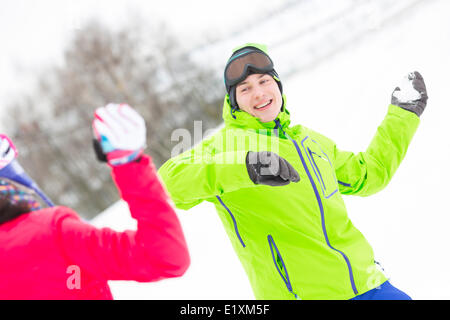 Felice giovane lanciando palle di neve verso la donna Foto Stock