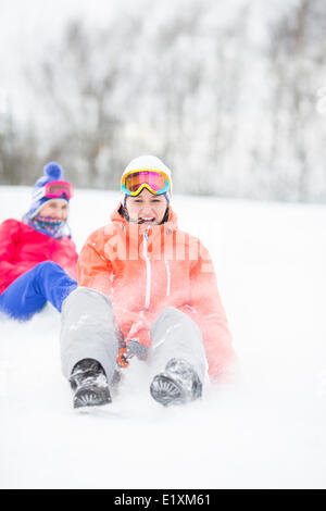 Giovane donna godendo di sled ride in neve con un amico in background Foto Stock