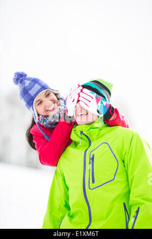 Sorridente giovane donna che copre lo sguardo dell'uomo in inverno Foto Stock