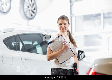 Ritratto di fiducia meccanico femmina con blocco per appunti in officina per auto Foto Stock